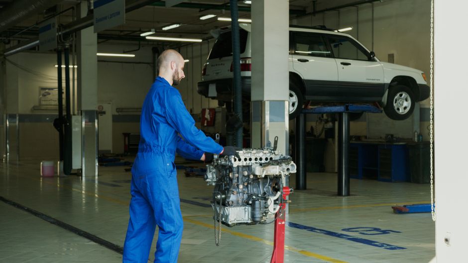 Mechanic in blue overalls working on an engine in an indoor automotive garage.